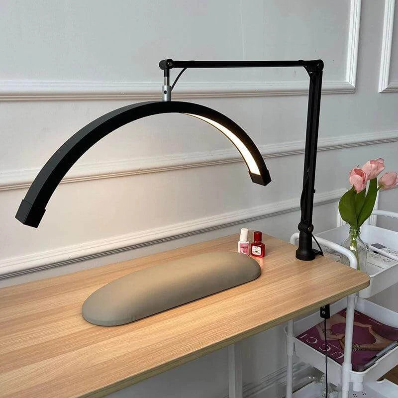 Arch nail table lamp with adjustable arm, LED fill lighting, placed on a manicure desk with beauty products and fresh flowers.